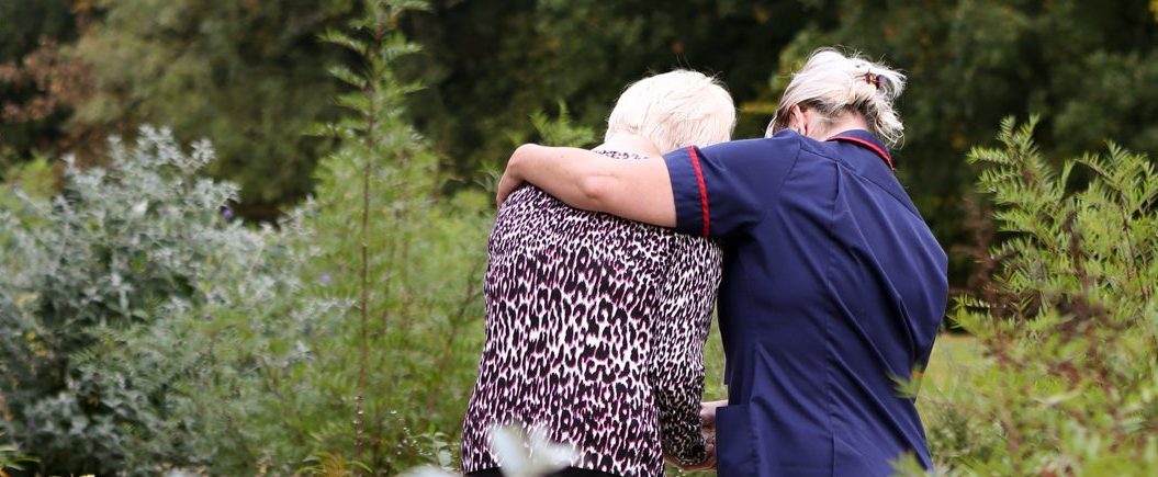 A hospice worker helping a woman walk through the garden
